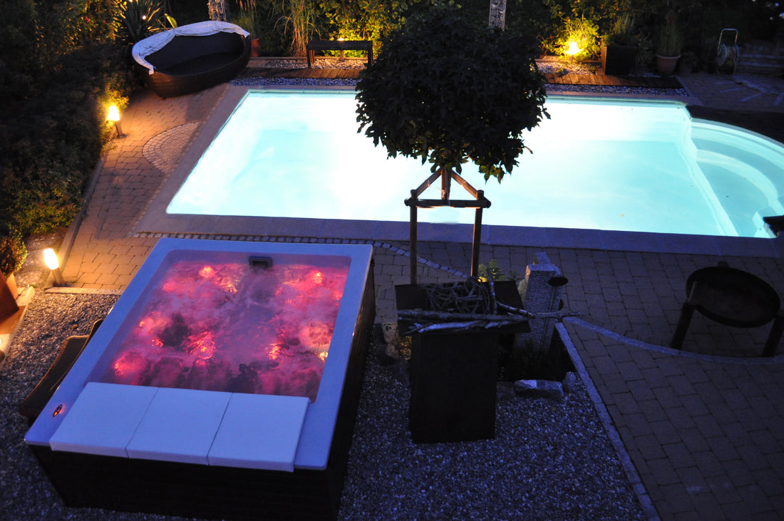 Bain d'hydromassage et piscine éclairés la nuit.