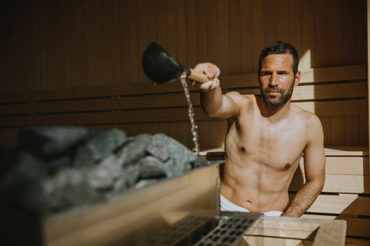 Homme versant de l'eau sur les pierres chaudes du sauna.