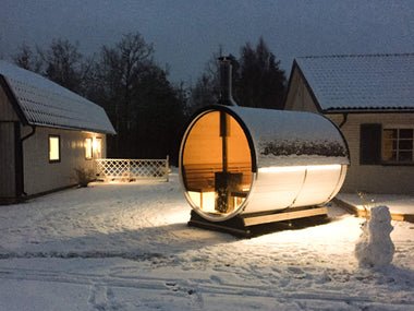 Sauna en tonneau dans un environnement enneigé avec éclairage intérieur.