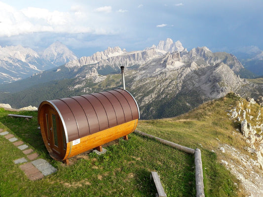 Sauna en tonneau sur une colline avec les montagnes en arrière-plan.