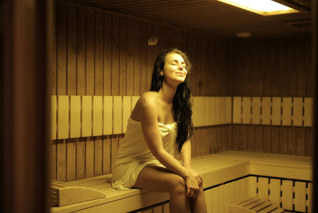 Femme assise sur un banc de sauna, couverte d'une serviette.