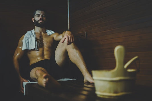 Un homme assis sur un banc dans un sauna avec un seau en bois à côté de lui.