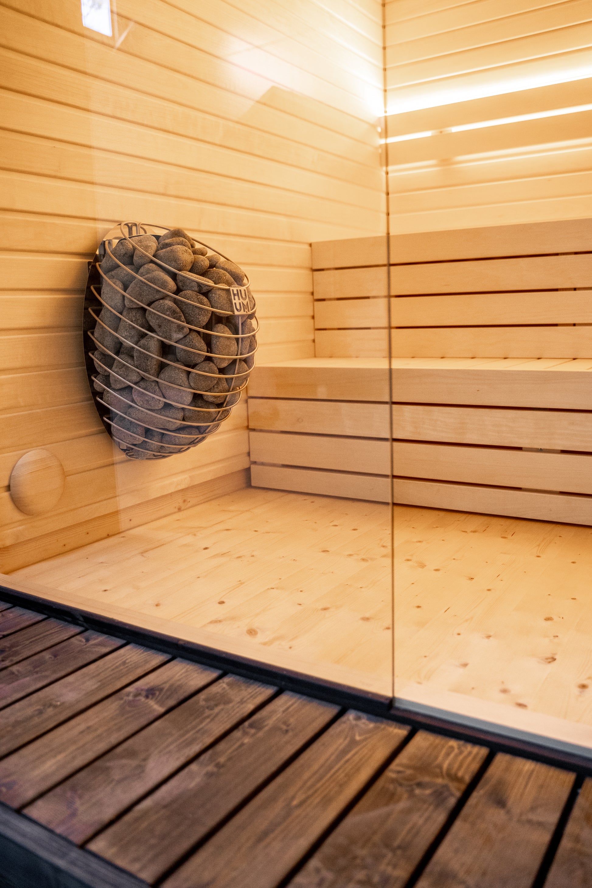 Sauna LUMI avec panier en pierre et paroi en verre.