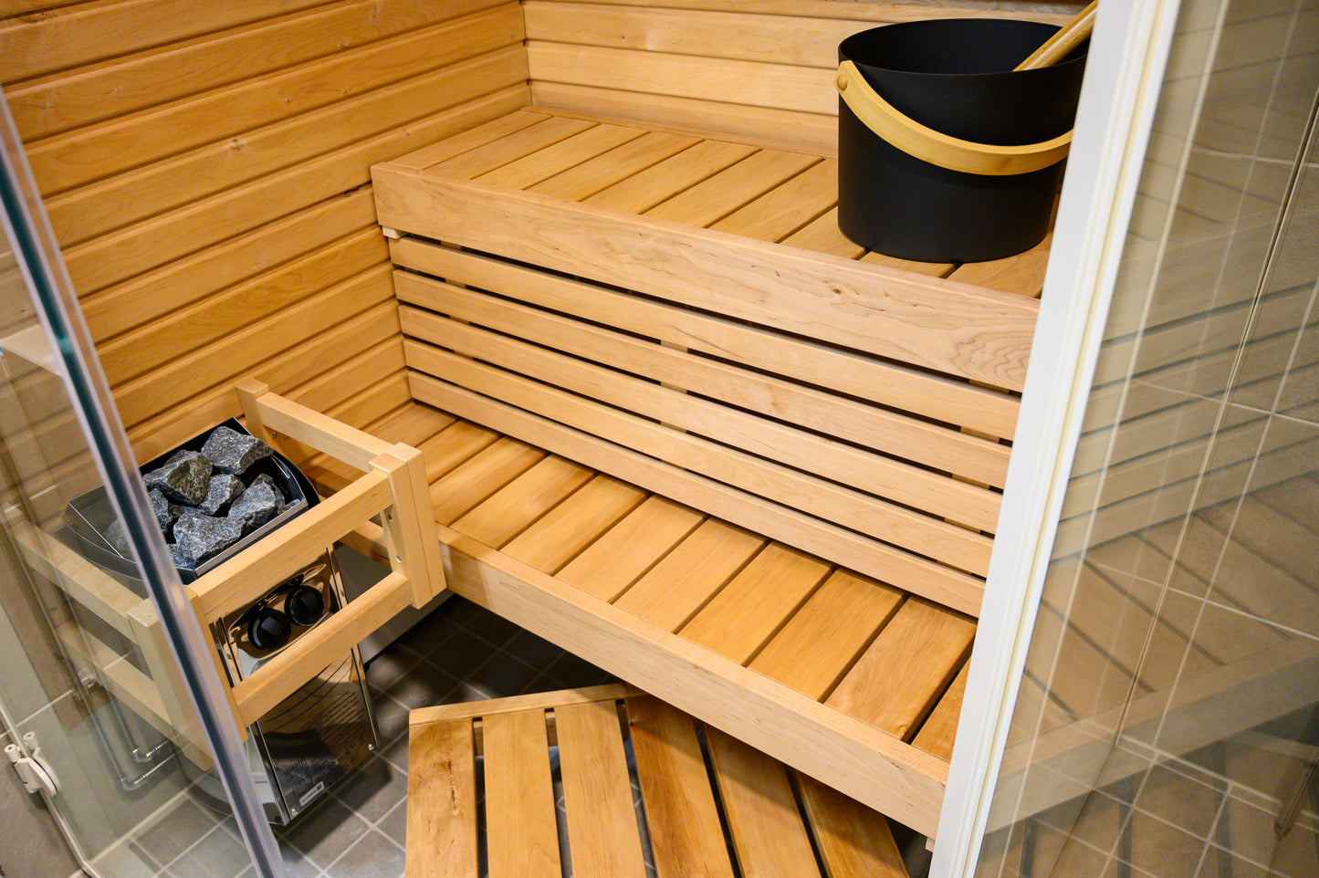 Sauna Sirius Corner avec bancs en bois et seau noir.