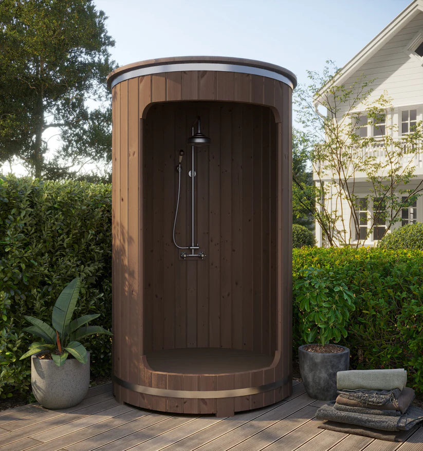 Douche extérieure en forme de tonneau avec des plantes tout autour.