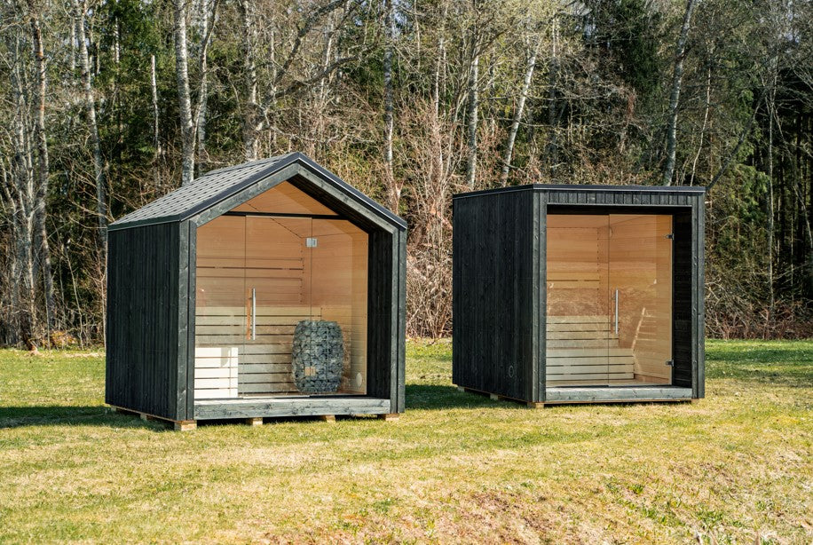 Sauna extérieur LUMI isolé avec une porte en verre, dans un espace vert.